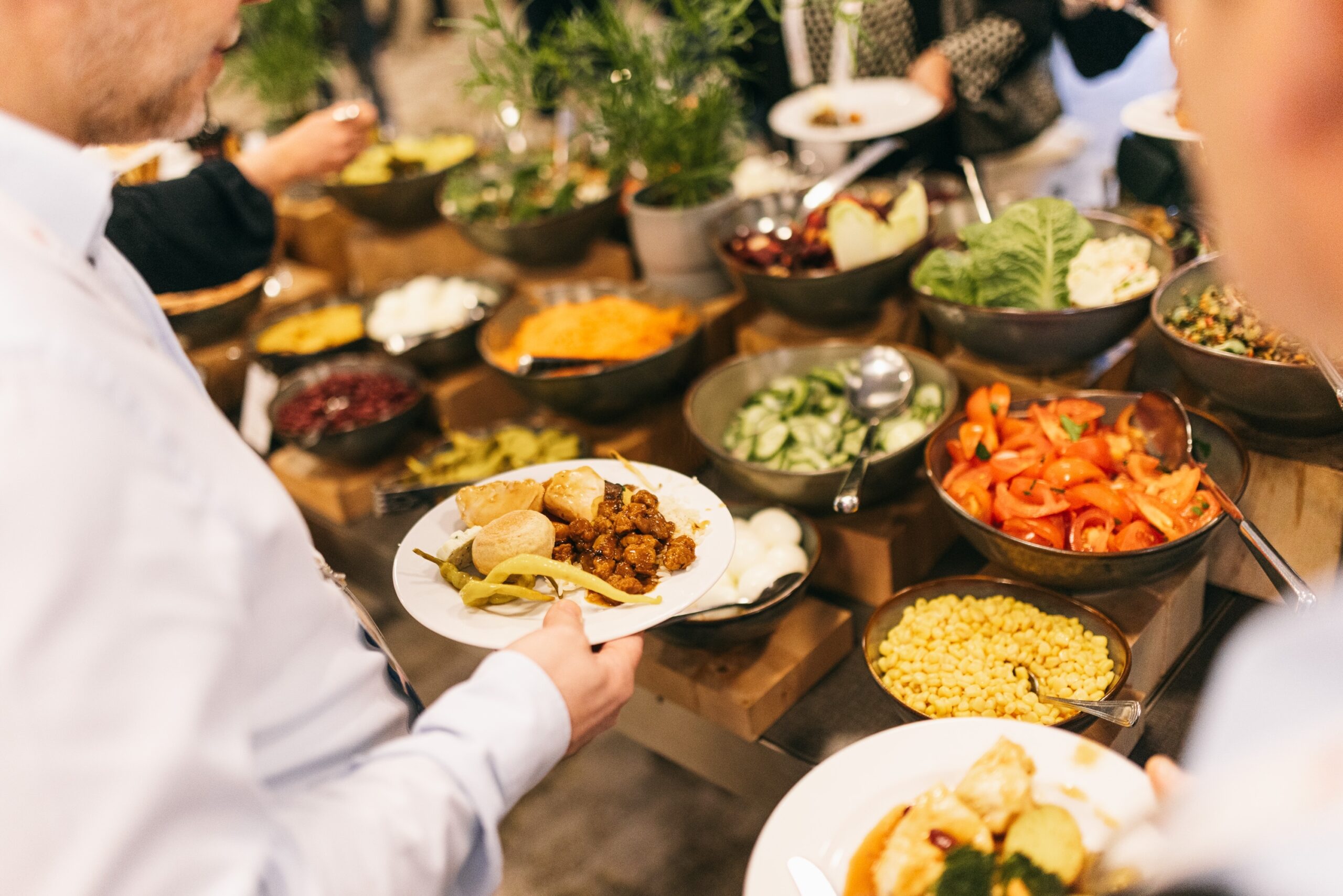 un uomo di fronte al tavolo di un buffet allestito da un catering aziendale, che tiene in mano un piatto di fritturine e antipadti