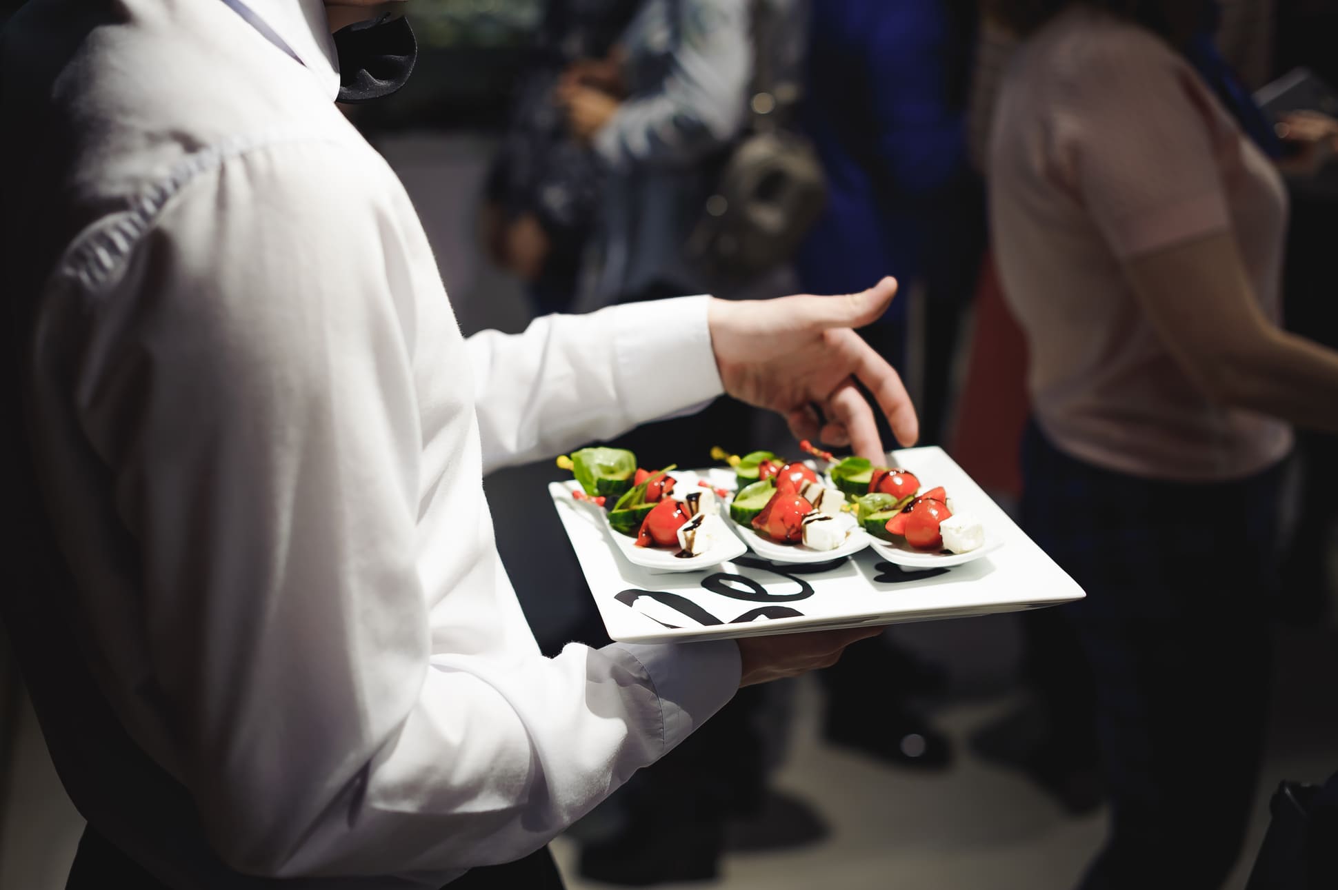 Cameriere catering inaugurazione aziendale Un cameriere in uniforme elegante porta un vassoio con finger food durante un’inaugurazione aziendale affollata.